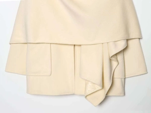 Detail of cream white wool coat featuring structured layered hem and clean pocket stitching