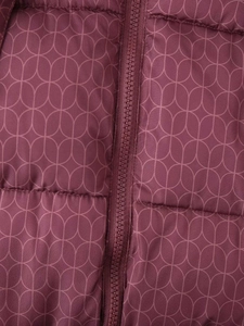 Détail d'une veste matelassée bordeaux avec motifs ovales roses et zip assorti
