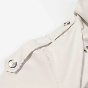 Detail shot of beige trench coat shoulder strap with dark button and neat stitching