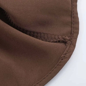 Macro shot of fine stitching and hem detail on dark brown woven midi dress fabric