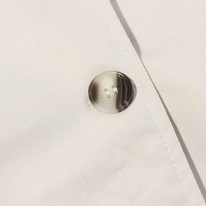 Macro detail of beige trench coat featuring a marble pattern resin button and fabric texture