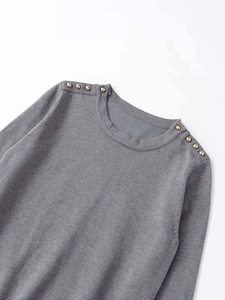 Detail of dark grey knit sweater showing golden decorative buttons on shoulder seams