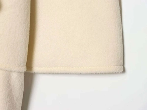 Detailed macro view of the beige wool coat hem showing soft fabric texture and neat stitching