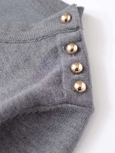 Detail of grey knitted sweater featuring decorative gold buttons on the shoulder seam
