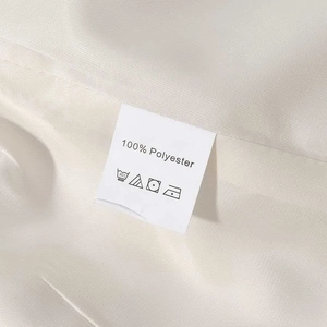 Detail of white laundry care label showing 100% Polyester fabric on light beige trench coat
