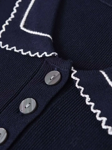Close-up of navy knit cardigan featuring white scalloped edges and lustrous buttons