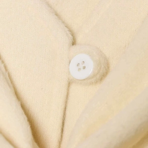 Close-up of a cream wool coat featuring a white resin button and soft plush texture