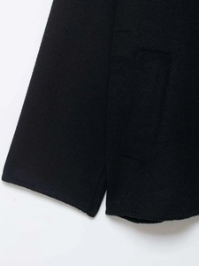 Detail view of black wool coat showing premium fabric texture and side slit stitching