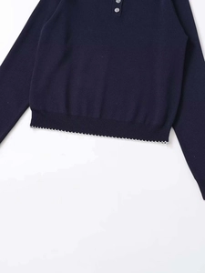Detailed close-up of navy knit sweater with white wavy crochet lace trim and ribbed hemline