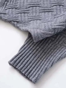 Macro detail of grey knit fabric showing basketweave texture and ribbed hem finishing