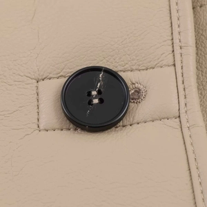 Detailed close-up of black four-hole button on beige textured faux leather jacket with stitching
