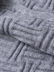 Close-up detail of grey knitted sweater showing geometric texture and soft warm fabric