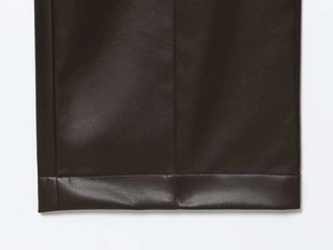 Détail des coutures verticales et de l'ourlet sur le pantalon en similicuir marron foncé
