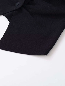 Detail shot of black knitted vest showing fabric texture and circular button closure