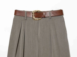 Detail showing high-waist wide-leg trousers with front pleats and a slim brown belt