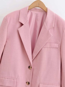 Close-up of pink blazer showing notched lapel, amber buttons, and woven fabric texture