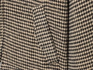 Macro shot of houndstooth jacket detail showing pocket stitching and metal zipper texture