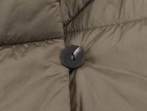 Detail of a round black button on a warm quilted olive green padded winter jacket