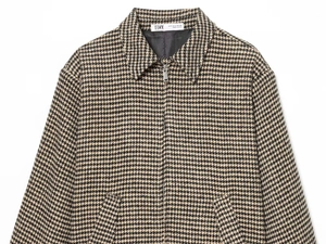 Close-up of houndstooth jacket detail with metal zipper and woven brand size label
