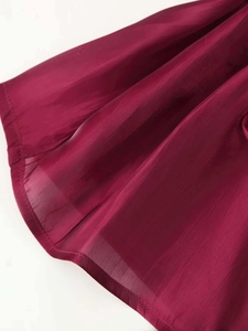 Close-up of burgundy glossy fabric featuring sheer tulle overlay and neat hemline detail