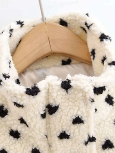 Detailed view of white fleece jacket featuring a black polka dot pattern and a front zipper