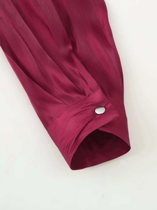 Detail of wine red pleated blouse sleeve with silver button and silky texture