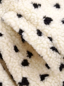 Close-up of soft white fleece jacket material featuring contrasting black polka dots
