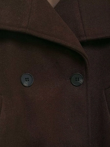 Detail of dark brown wool coat showing high-density fabric texture and black buttons
