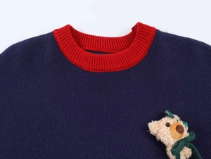 Détail du pull en tricot bleu marine avec col rouge et petit ours en peluche 3D