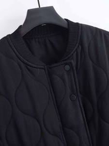 Detail view of wave-quilted black jacket featuring ribbed collar and snap buttons