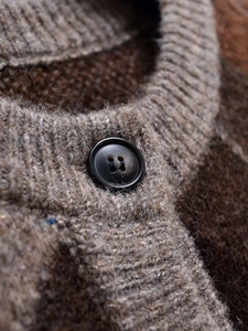 Macro view of textured knit fabric with resin button detail on a brown cardigan