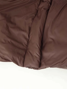 Detailed close-up showing brown quilted fabric and precise vertical stitching of the coat
