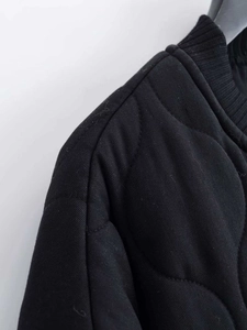 Macro detail of black quilted jacket shoulder showing twill fabric and ribbed knit collar