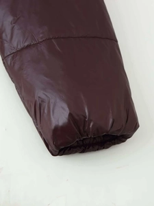 Detailaufnahme der elastischen Bündchen und glänzenden Nylon-Pufferjacke in Burgunder