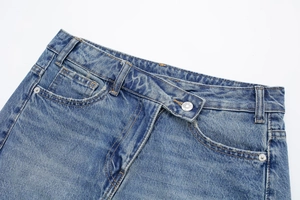 Détail de la jupe en jean bleu clair avec taille asymétrique et poches à rivets