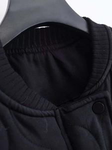 Detail of black quilted jacket neckline with elastic ribbed trim and matte snap button