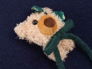 Gros plan d'un charm ours 3D avec ruban vert sur un pull en maille bleu marine