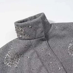 Detail von glitzernden Silberpailletten und Perlenstickerei auf einer grauen Wolljacke