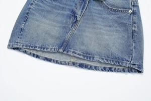 Détail d'une jupe en jean bleu montrant des rivets métalliques et la texture délavée