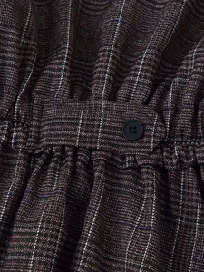 Detailed close-up of plaid fabric texture with elastic gathers and a black button
