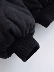 Close-up of black quilted jacket cuff featuring elastic ribbed knit and durable twill fabric