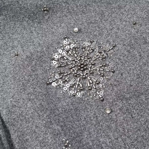 Detailaufnahme aus grauem Wollstoff mit silbernen Perlen und Pailletten-Blumenstickerei