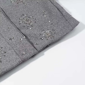 Detailaufnahme von grauem Wollstoff mit silbernen Pailletten und weißen Perlenstickereien