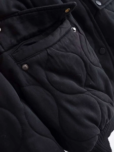 Detail of black quilted winter jacket with unique wavy stitching and metallic buttons