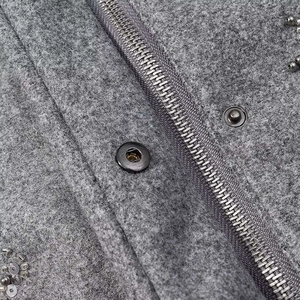 Detailansicht der Wollstofftextur mit Pailletten und Metallreißverschluss an grauer Jacke