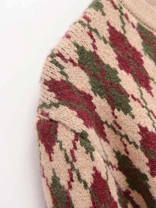 Detail of a thick diamond pattern knit cardigan featuring beige, red and green yarn textures