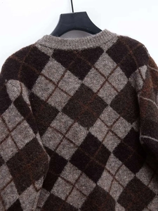 Detail shot of a dark brown argyle knit sweater showing the crew neck and wool texture