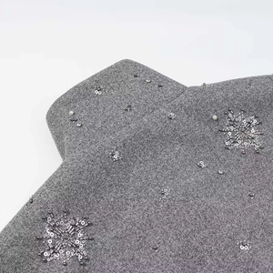 Detailansicht eines grauen Wollmantels mit handgenähten Pailletten und Perlen-Schneeflocken