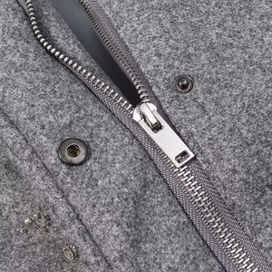 Detaillierte Makroansicht von Silberreißverschluss und Metallknöpfen auf grauem Wollmantel