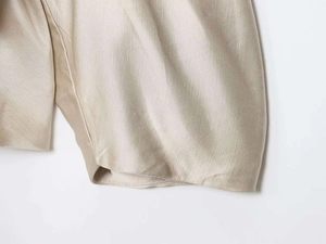 Close-up of champagne gold satin fabric texture with neat hem stitching on women shirt